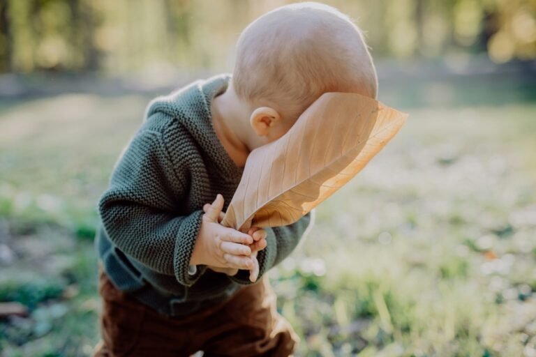 Little baby hiding his face behind a leaf.