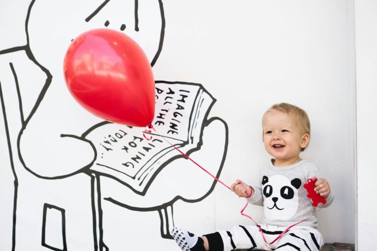 Smiling baby holding a red ballon.