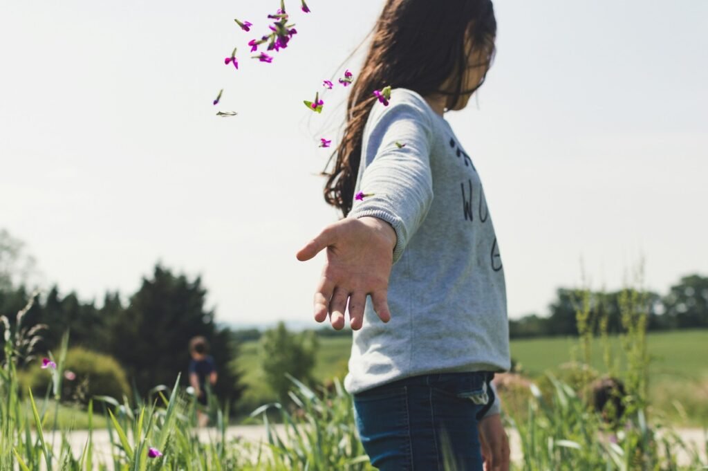 A girl is standing on a green grass field at daytime.